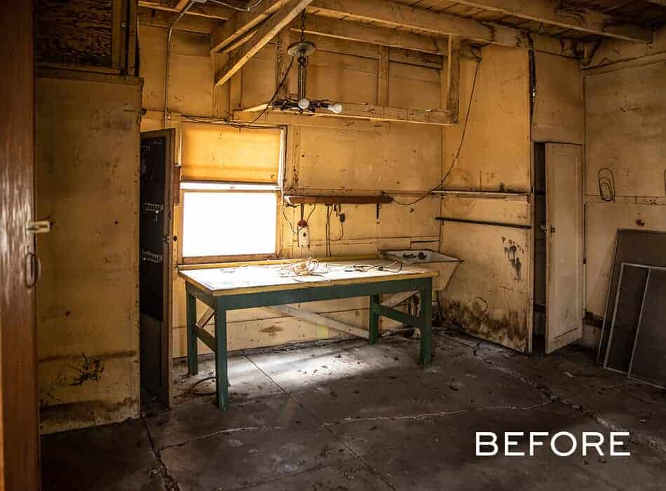 A before image of an old, worn-out workshop with peeling walls, exposed beams, and a single workbench under dim lighting