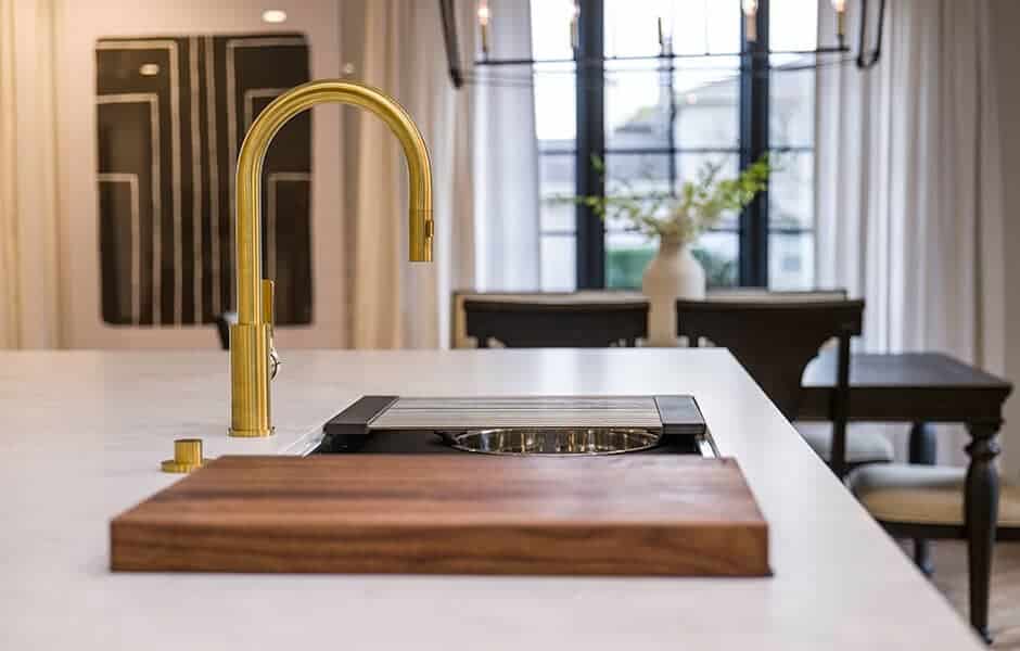 Stainless steel kitchen sink with a wooden cutting board and white ceramic bowl inside