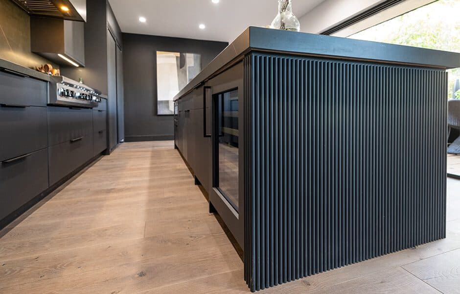 Modern kitchen with sleek black cabinetry, fluted island, and wood flooring