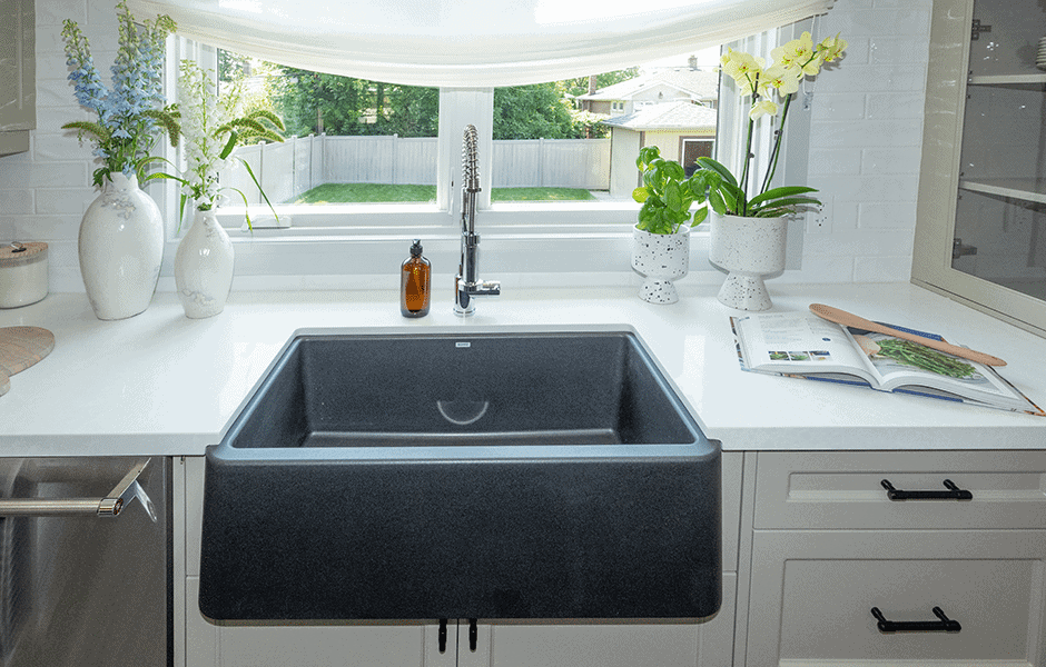 Bright kitchen sink area with a black farmhouse sink, white countertop, plants, and large window overlooking a yard