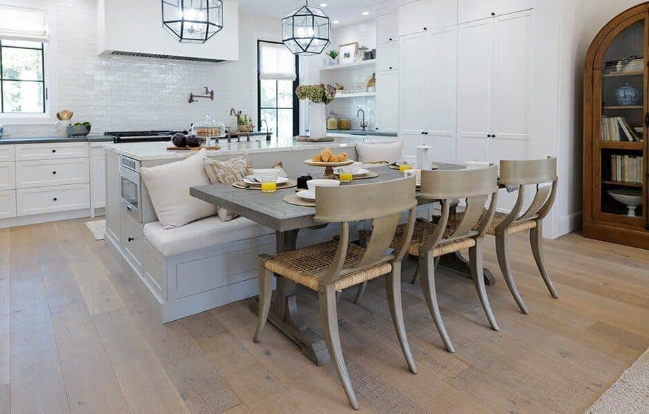 Bright kitchen-dining area with built-in bench, wooden table, white cabinetry, and pendant lighting