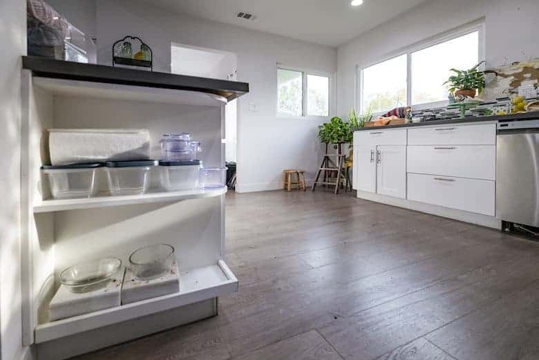 Spacious kitchen with white cabinets, open shelving, plants, and natural light on wood floors