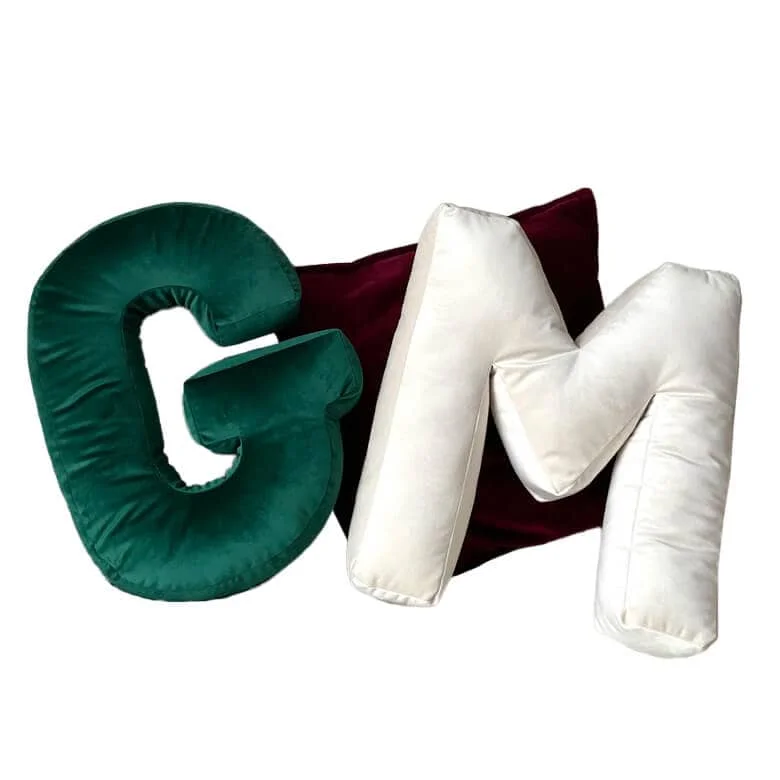 Letter-shaped pillows, "G" in green and "M" in white, with a burgundy cushion in the background