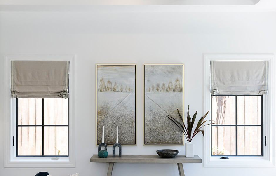 Minimalist room with framed art, a wooden console table, and decor between two windows.