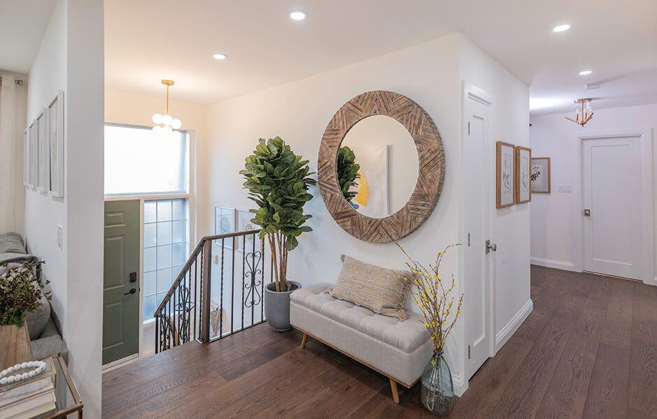 Bright entryway with a round wooden mirror, bench, potted plant, and hardwood flooring