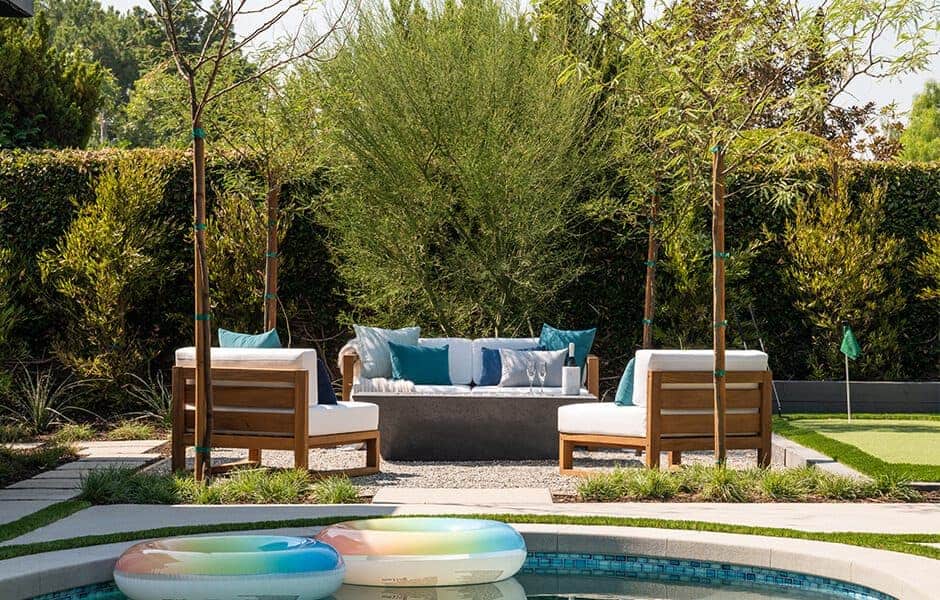 Outdoor seating with wooden furniture, blue cushions, and greenery near a pool