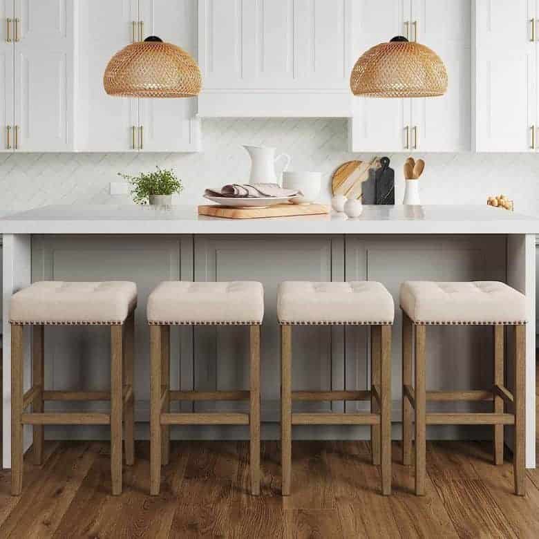 Four beige upholstered counter stools with wooden frames around kitchen island with white countertop