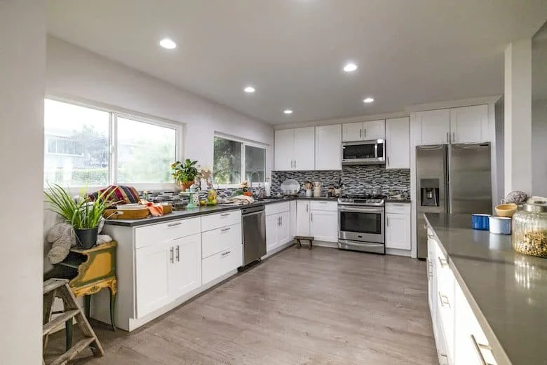 Spacious kitchen with white cabinets, stainless steel appliances, and light wood floors