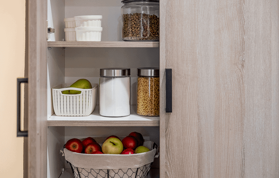 Organized pantry with glass jars, fresh apples, and a basket of green pears on neatly arranged shelves