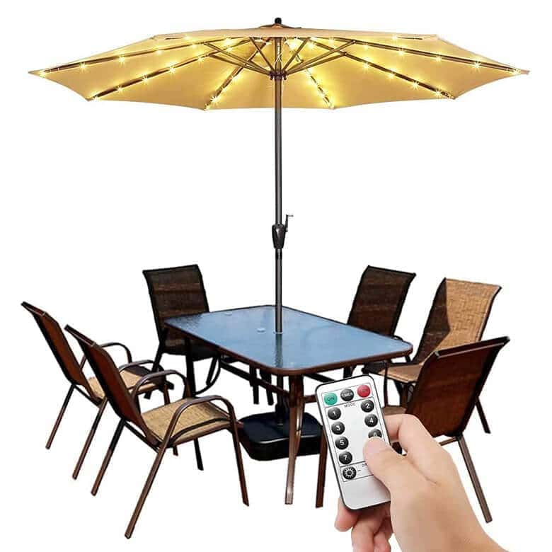 Patio set with a glass table, six brown chairs, and a lighted umbrella, with a hand holding a remote control