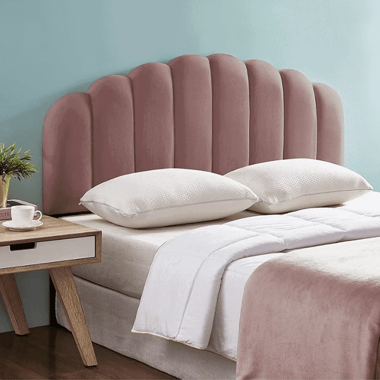 A pink velvet headboard with a scalloped design, positioned behind a bed with white bedding