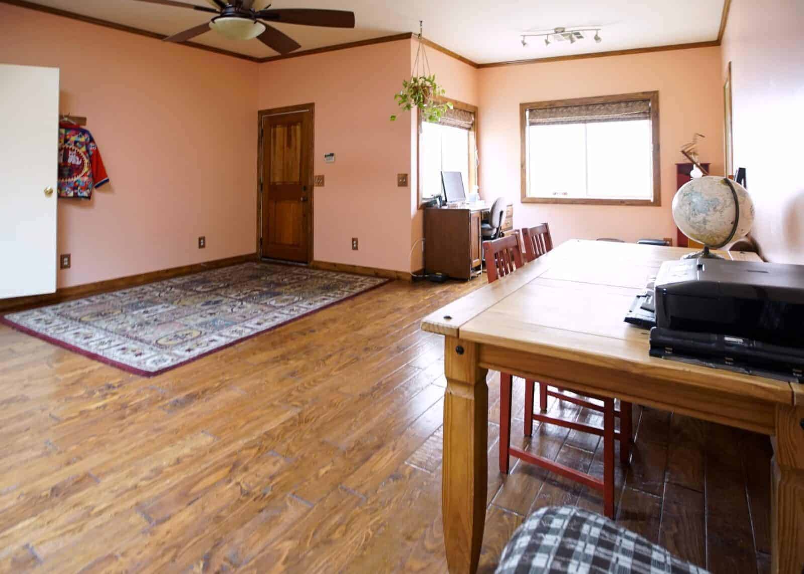 Spacious room with wooden flooring, a large rug, a wooden table with chairs, a globe, and a work desk near a window