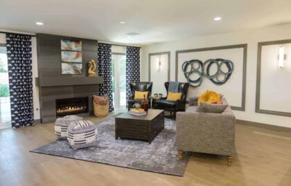 Living room with a gray fireplace, a large abstract artwork above it, and a comfortable seating arrangement with a sofa, armchairs, and ottomans