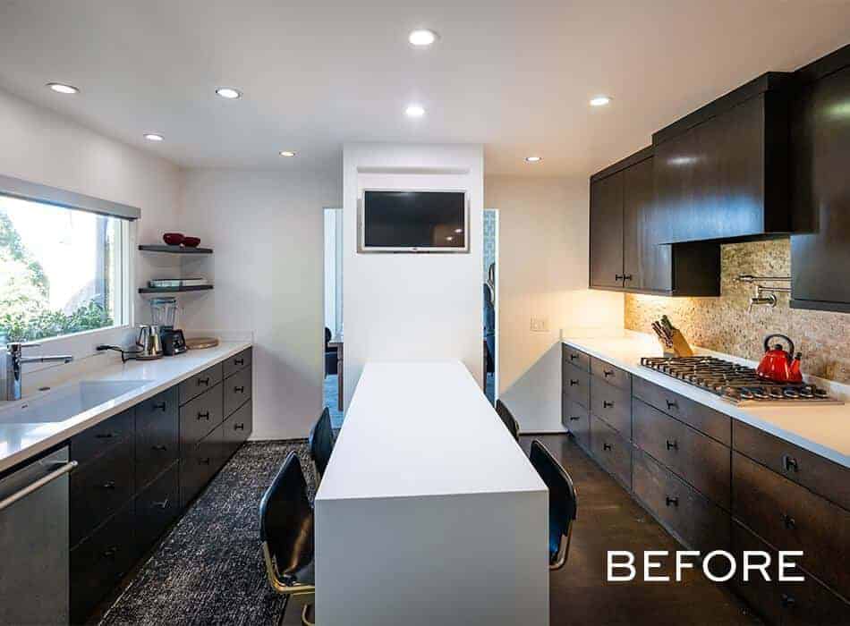 An before image of a kitchen with dark wood cabinets, white countertop, mounted TV, and a spacious layout.