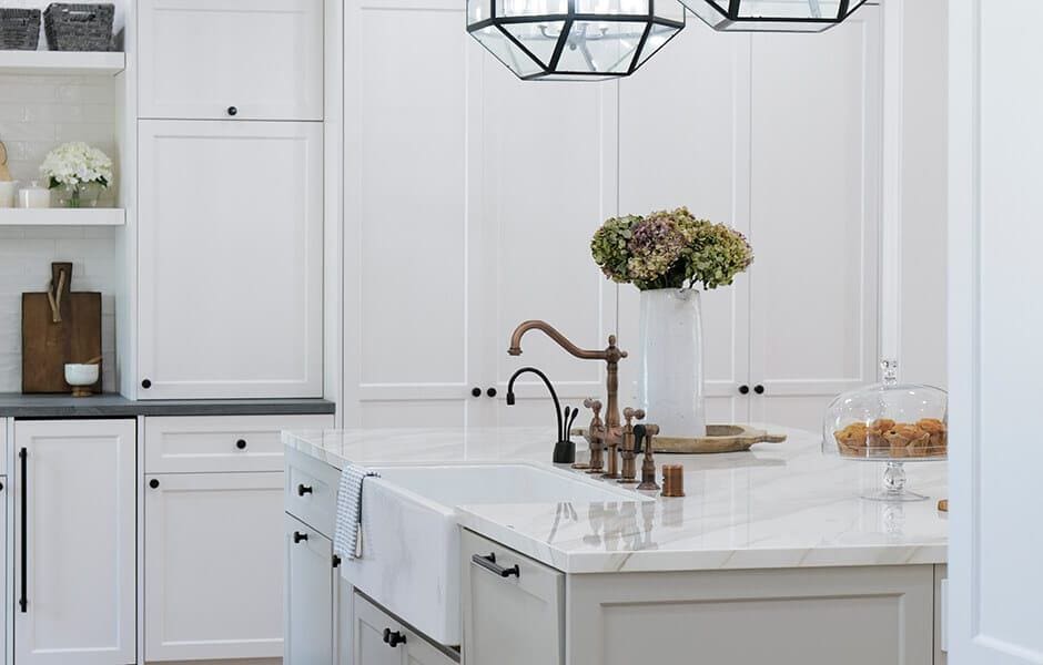 Bright kitchen with white cabinetry, marble island, vintage-style faucet, and decorative flowers and pastries