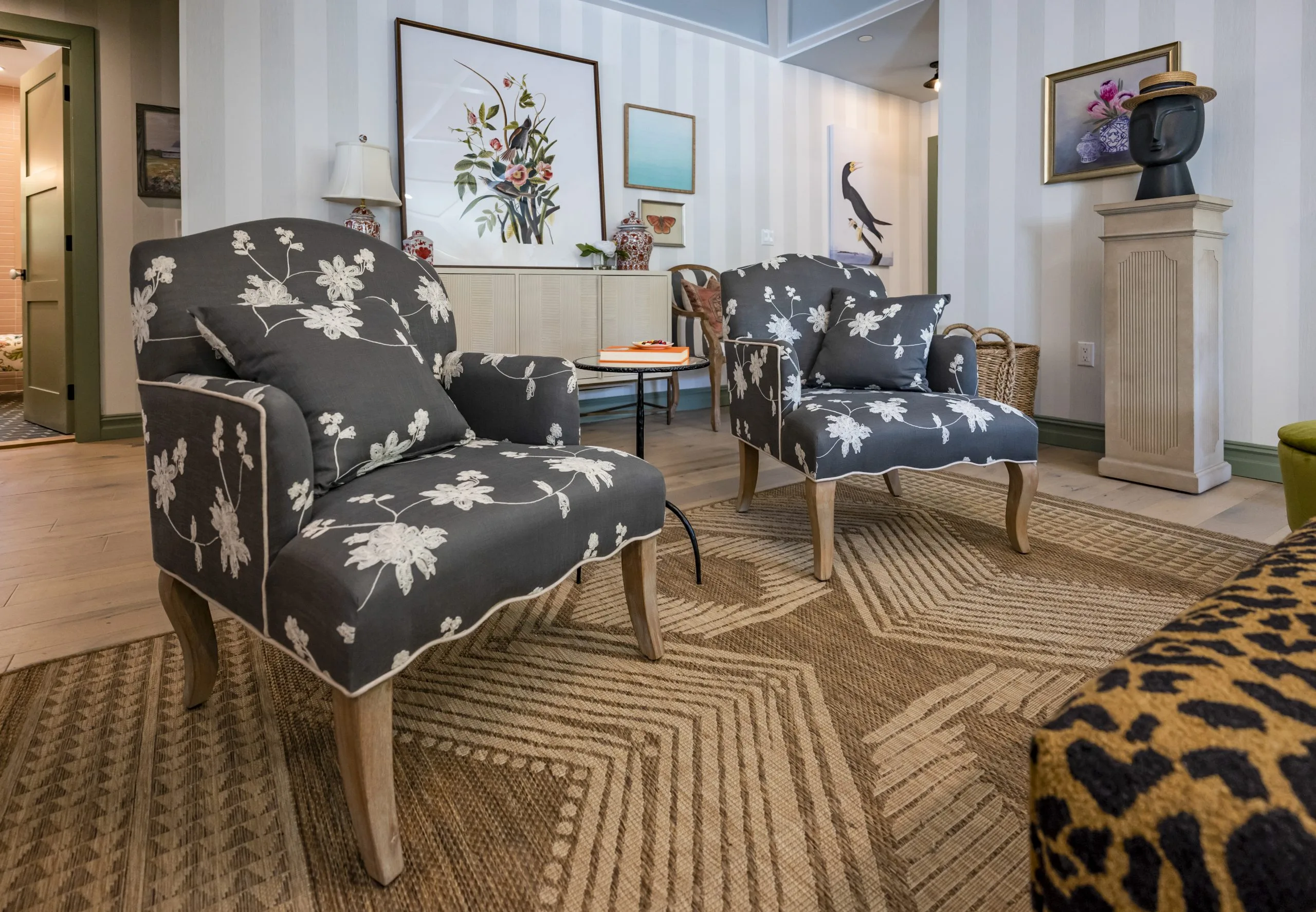 Living room with bohemian decor featuring floral armchairs, jute rug, leopard ottoman, and a round table with book and coffee